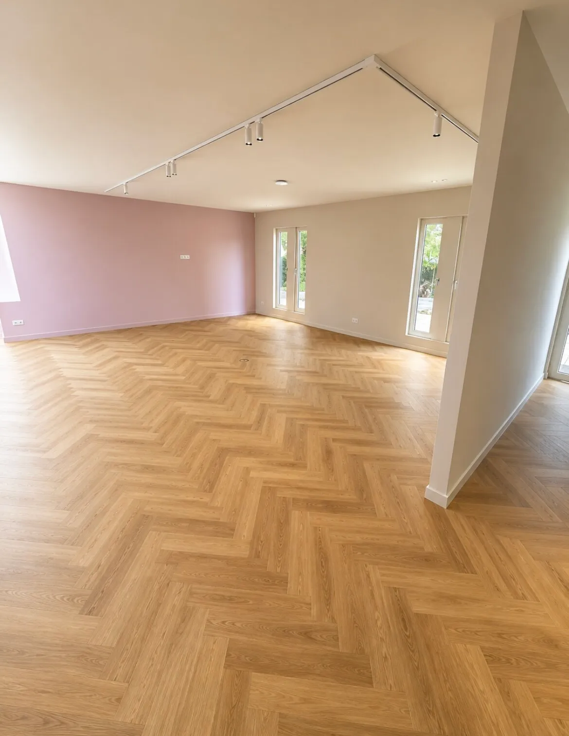 Lichte woonkamer met roze accentwand, visgraatvloer tot aan de tuindeuren